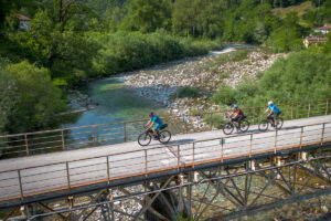 Cyclists riding over bridge over Natisone river.
